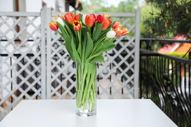 Photo of Beautiful colorful tulips in glass vase on white table at balcony