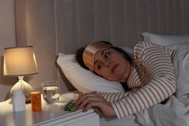 Photo of Mature woman taking pills from nightstand in bedroom at night. Insomnia concept
