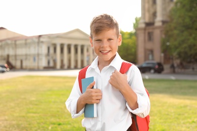 Photo of Little boy with backpack and notebook outdoors. Stationery for school