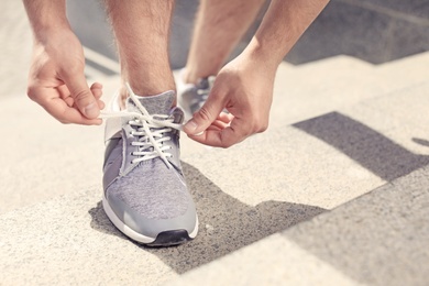 Photo of Young man tying shoelaces on his sneakers outdoors, closeup