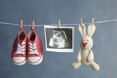 Photo of Pair of child's booties, ultrasound photo and toy bunny hanging on laundry line against dark background