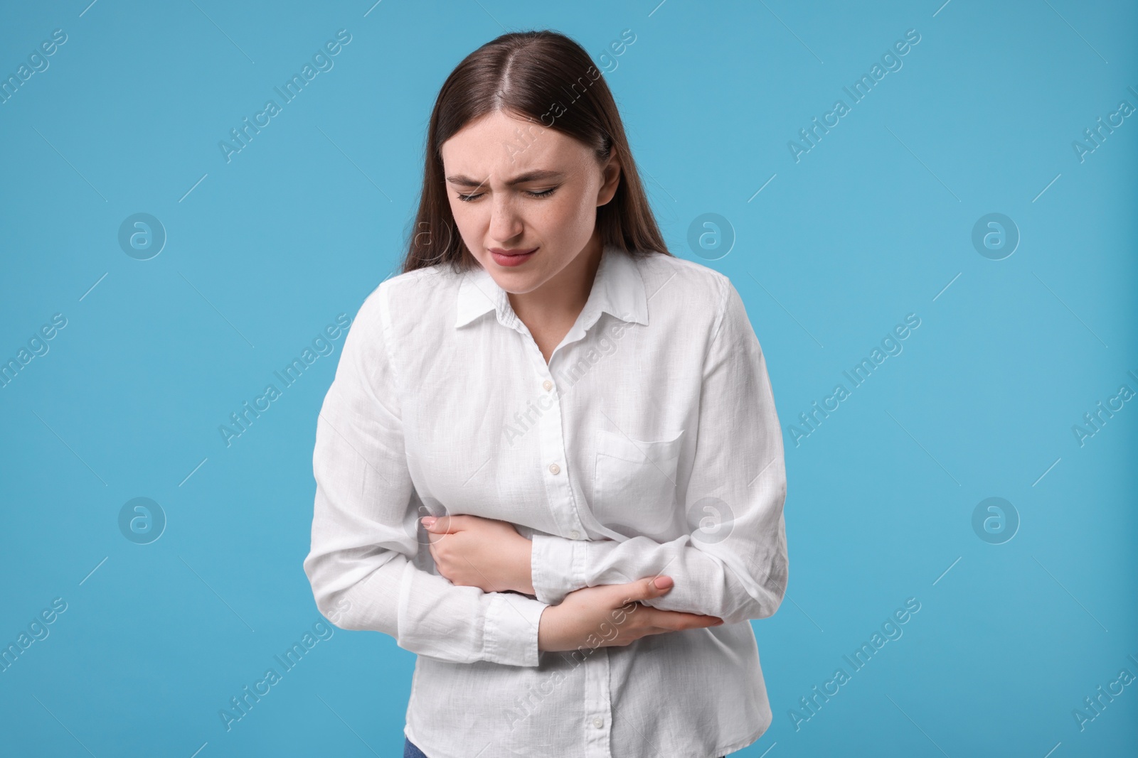 Photo of Young woman suffering from stomach pain on light blue background
