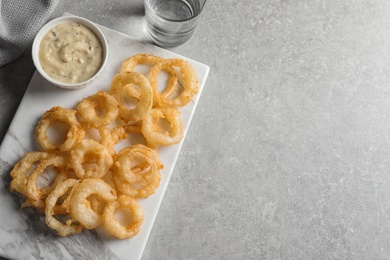 Flat lay composition with delicious crispy onion rings and sauce on light background. Space for text