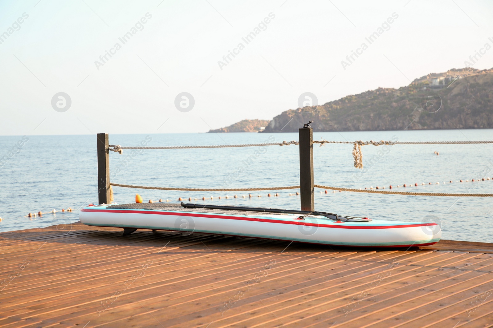 Photo of SUP board with paddle on wooden pier near sea