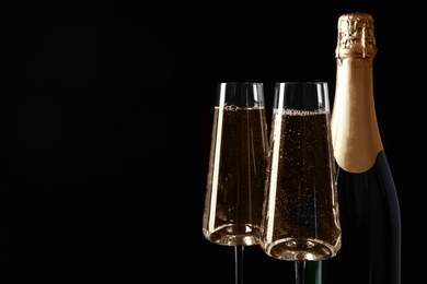 Bottle and glasses of champagne on black background, space for text