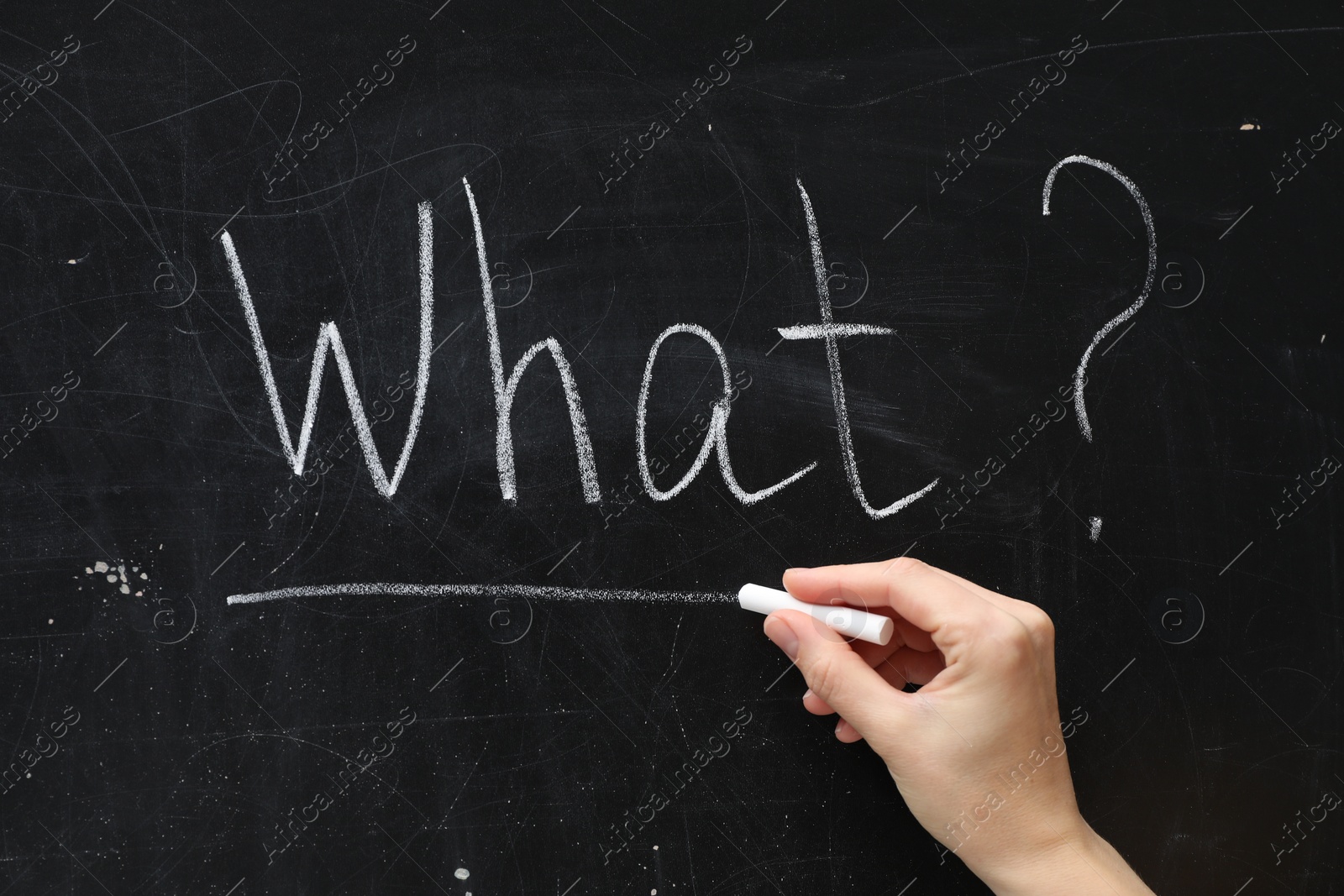 Photo of Woman writing word What? with chalk on blackboard, closeup