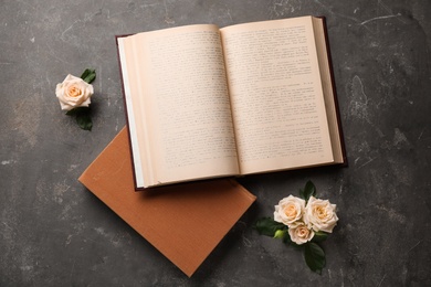 Photo of Open hardcover book and flowers on grey stone background, flat lay