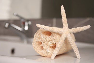 Natural loofah sponge and starfish on washbasin in bathroom, closeup. Space for text