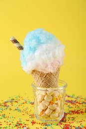 Photo of Sweet cotton candy in waffle cone on yellow background, closeup