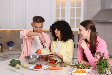 Friends cooking healthy vegetarian meal at white marble table in kitchen