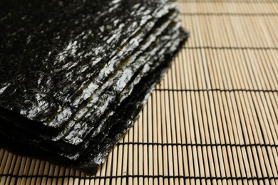 Stack of dry nori sheets on bamboo mat, closeup. Space for text