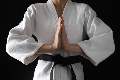 Photo of Man in keikogi with black belt on dark background, closeup. Martial arts uniform