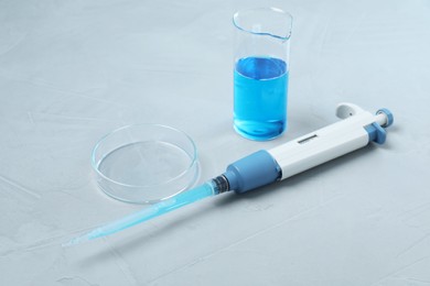 Photo of Laboratory analysis. Micropipette, beaker with liquid and petri dish on grey table