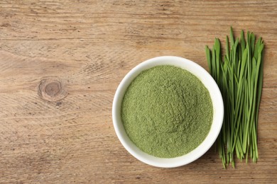 Photo of Wheat grass powder in bowl and fresh green sprouts on wooden table, flat lay. Space for text