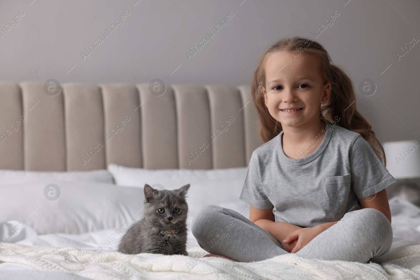 Photo of Cute little girl with kitten on bed at home. Childhood pet