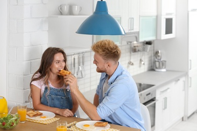 Happy young couple having breakfast at table in kitchen
