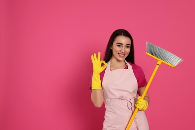 Photo of Beautiful young woman with broom showing OK gesture on pink background. Space for text