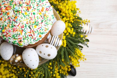 Traditional Easter cake with sprinkles, painted eggs and beautiful spring flowers on white wooden table, top view