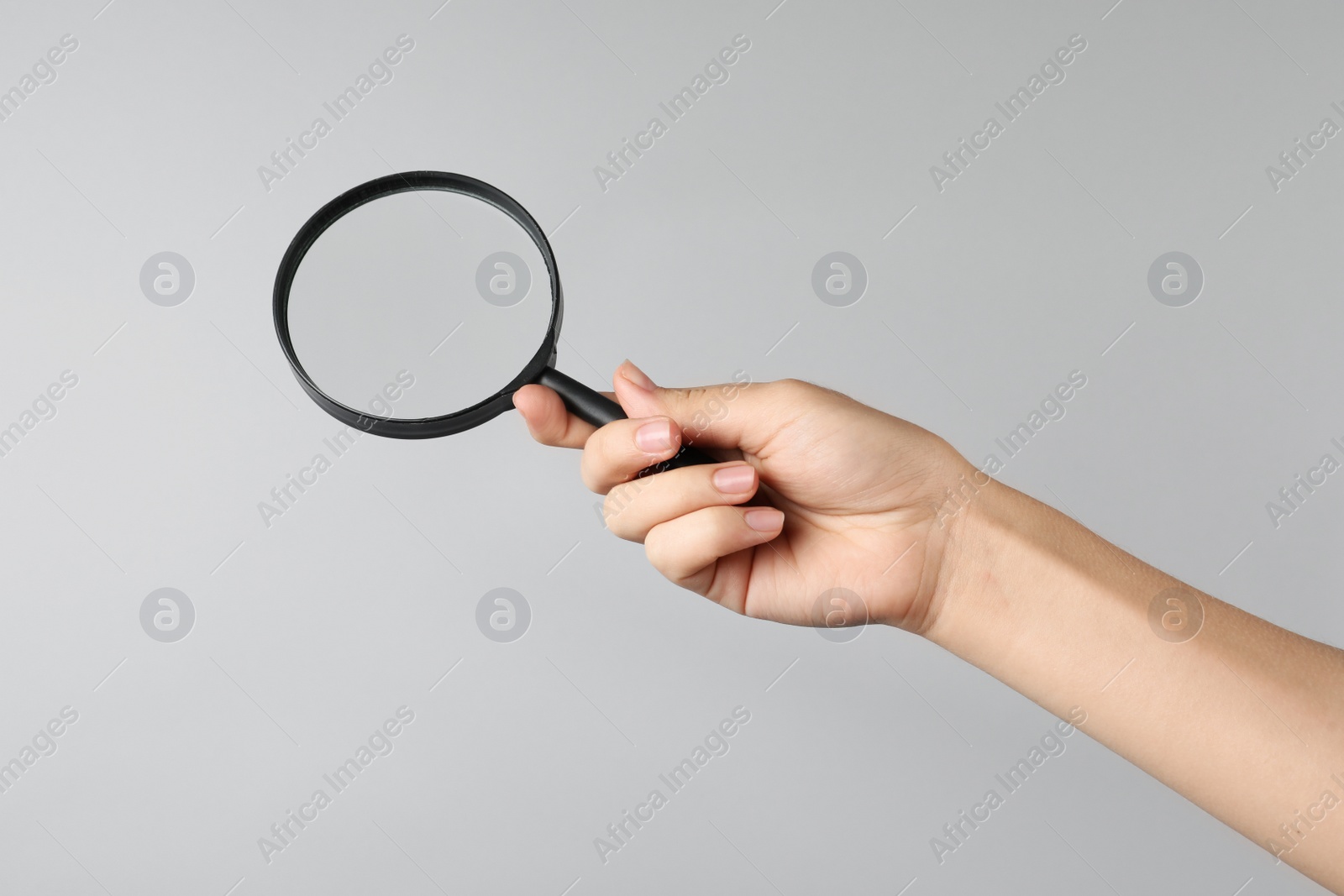 Photo of Woman holding magnifying glass on grey background, closeup. Find keywords concept