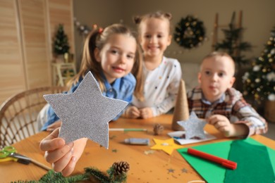 Photo of Cute little children at table indoors, focus on hand with star. Making Christmas decor
