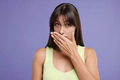 Photo of Embarrassed woman covering mouth with hand on violet background