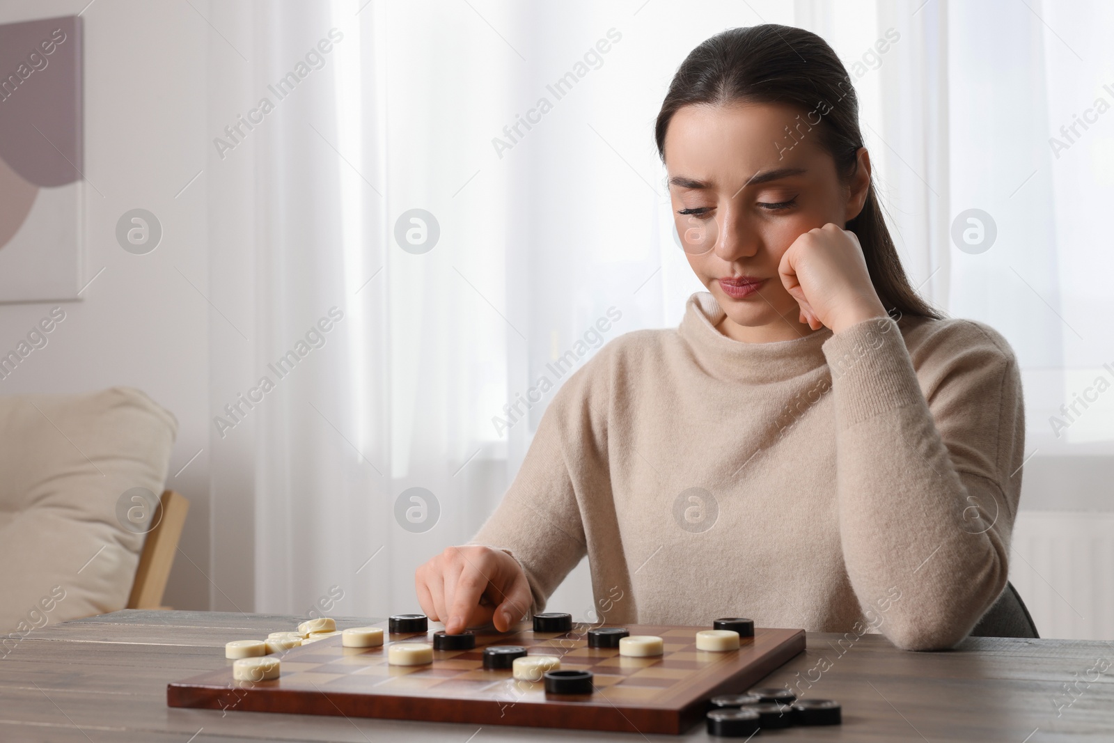 Photo of Playing checkers. Concentrated woman thinking about next move at table in room, space for text