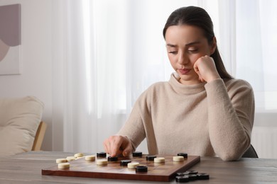 Photo of Playing checkers. Concentrated woman thinking about next move at table in room, space for text