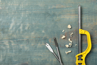 Photo of Small hand saw, spade drill bits and shavings on blue wooden background, flat lay with space for text. Carpenter's tools