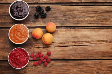 Different puree in bowls and fresh fruits on wooden table, flat lay. Space for text