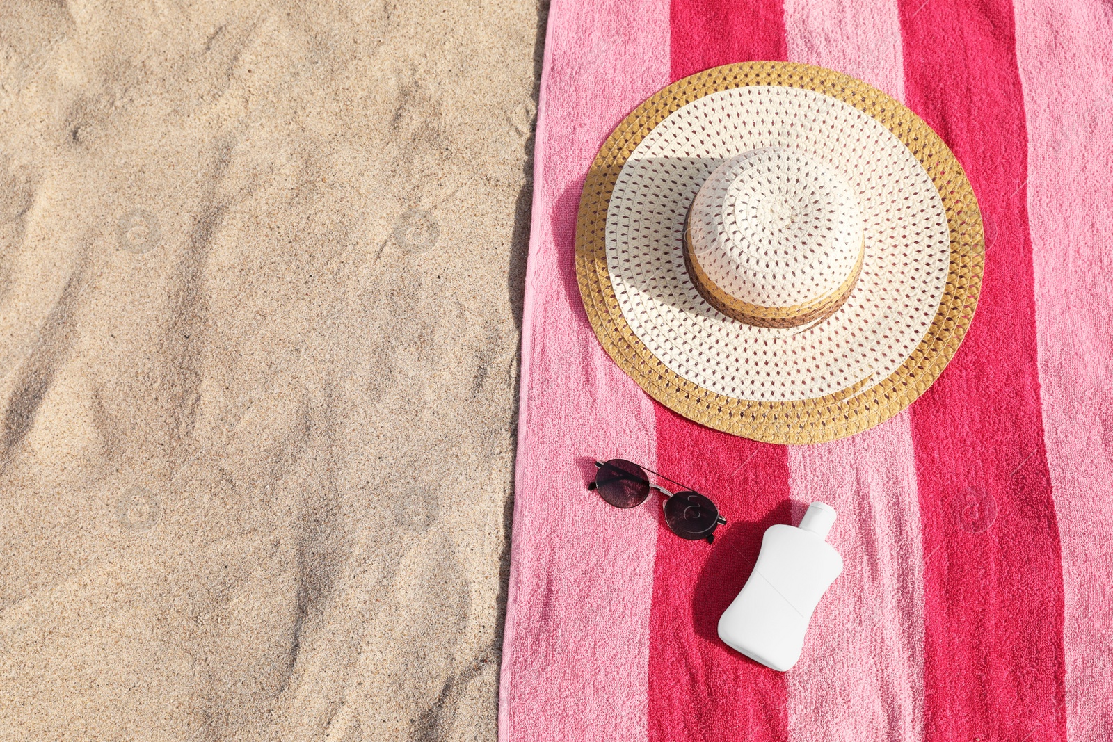 Photo of Beach towel with straw hat, sunglasses and sunscreen on sand, flat lay. Space for text