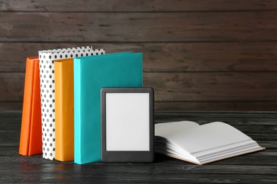 Photo of Modern e-book reader and hard cover books on black wooden table