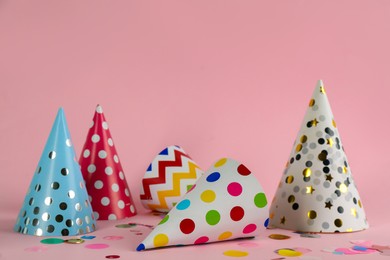 Photo of Colorful party hats and confetti on pink background. Space for text