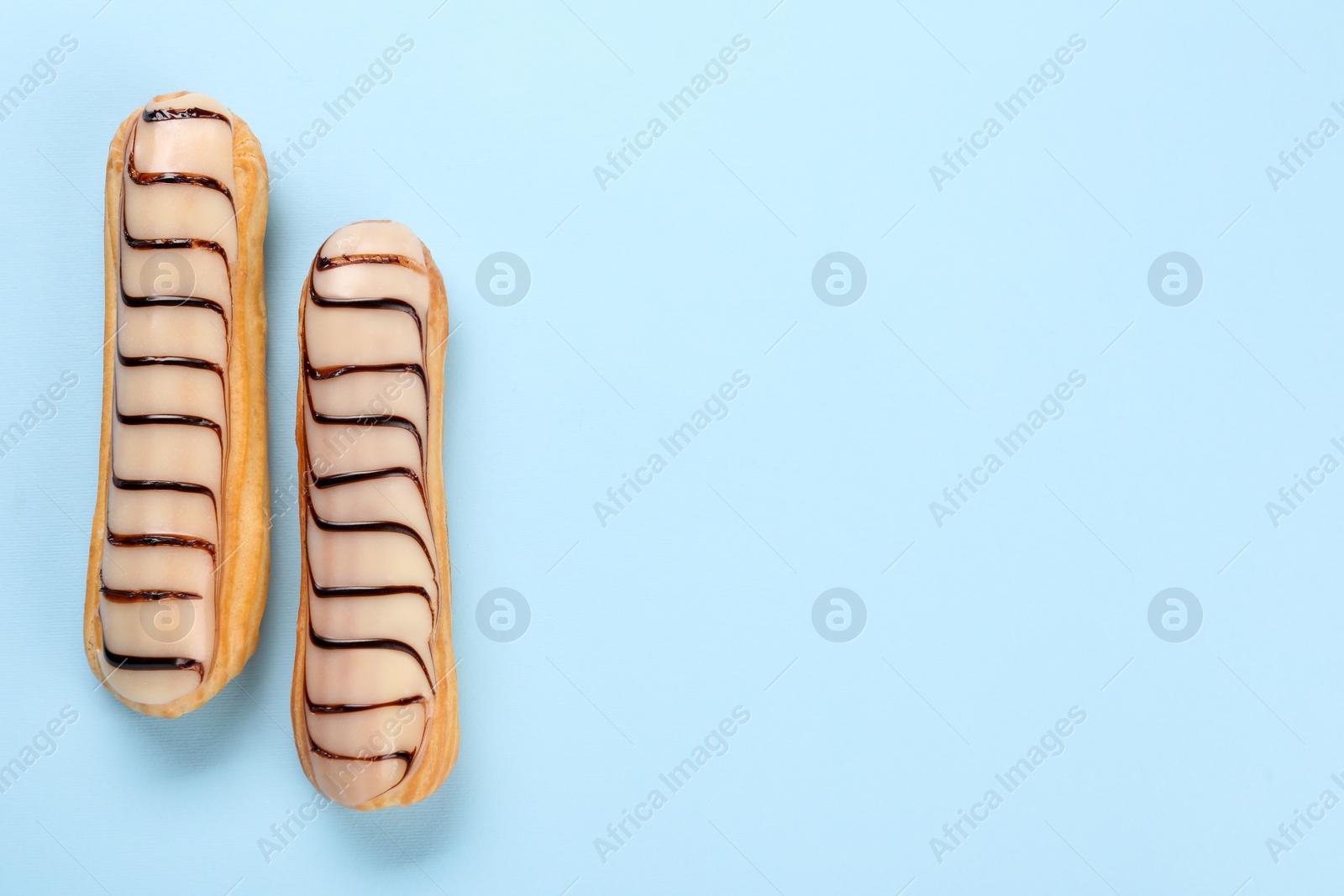 Photo of Delicious eclairs covered with glaze on light blue background, top view. Space for text