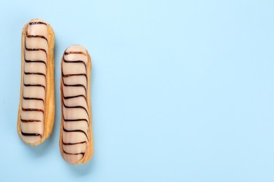 Photo of Delicious eclairs covered with glaze on light blue background, top view. Space for text