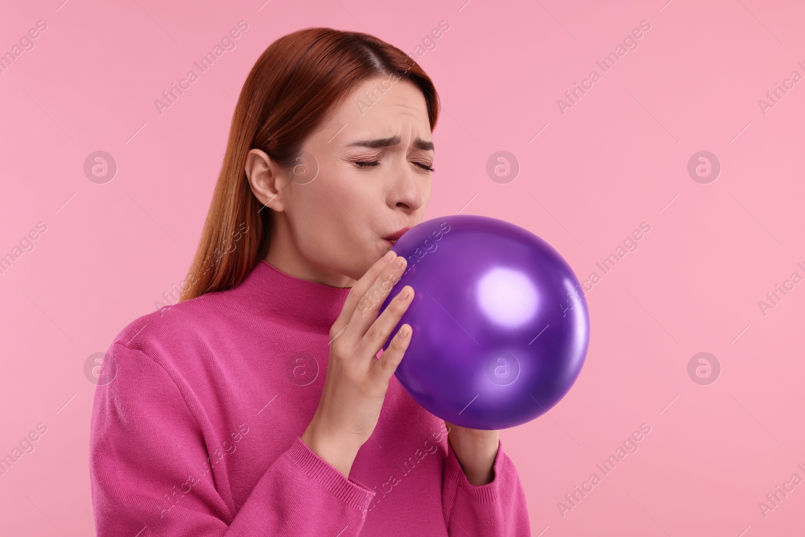 Photo of Woman inflating purple balloon on pink background