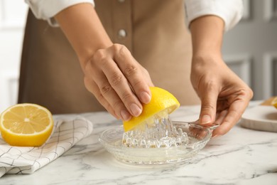 Woman squeezing lemon juice at white marble table, closeup