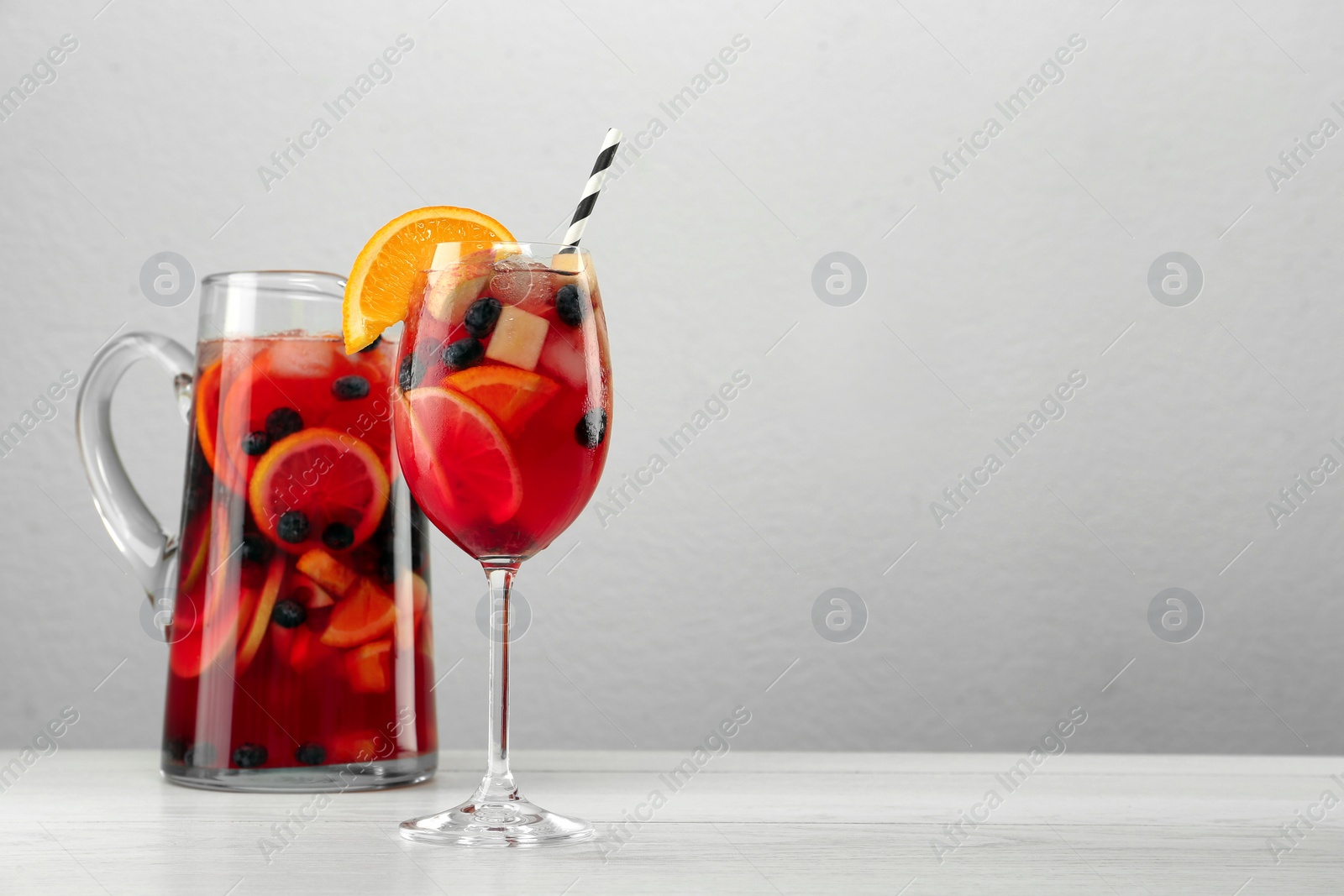 Photo of Glass and jug of Red Sangria on white wooden table against light grey background. Space for text