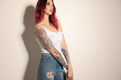 Beautiful woman with tattoos on arms against light background