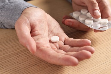 Man holding pills at wooden table, closeup