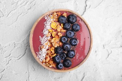 Photo of Bowl of delicious fruit smoothie with fresh blueberries, granola and coconut flakes on white textured table, top view