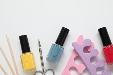 Photo of Nail polishes, orange sticks, scissors and toe separators on white background, flat lay. Space for text