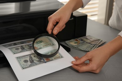Photo of Counterfeiter examining sheet of paper with dollar banknotes at table indoors, closeup. Fake money concept