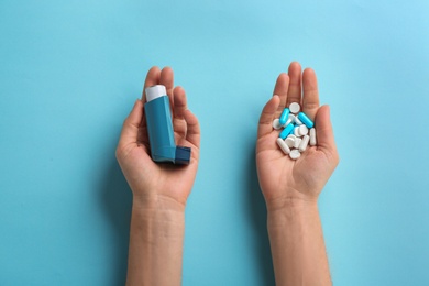 Photo of Woman holding asthma inhaler and pills on color background, top view