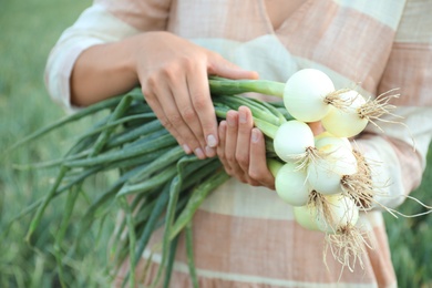 Photo of Woman holding fresh green onions outdoors, closeup