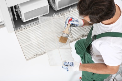 Young male technician cleaning air conditioner indoors