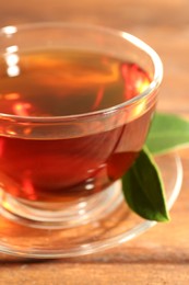 Photo of Aromatic tea in glass cup and green leaves on wooden table, closeup