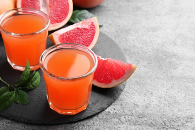 Photo of Tasty freshly made grapefruit juice and fruit on grey table. Space for text