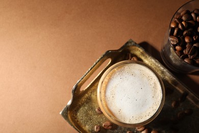 Aromatic coffee with milk in glass and beans on brown table, flat lay. Space for text