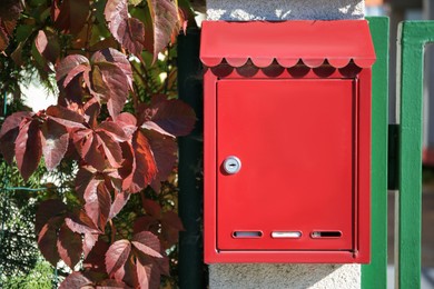 Photo of Red metal letter box on stone column near gate outdoors