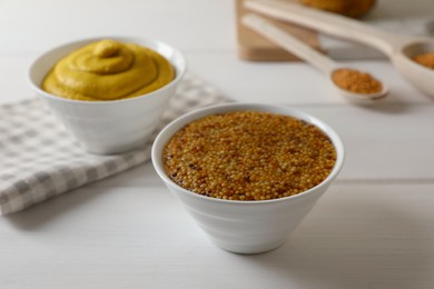 Bowls of whole grain mustard on white wooden table